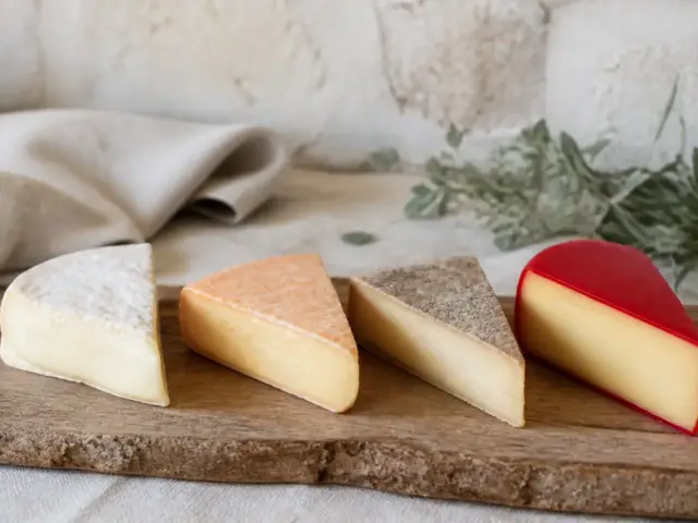 Plusieurs fromages coupés montrant leur croûte : un duvet blanc, une croûte orangée, une croûte grise et une enveloppe de cire rouge
