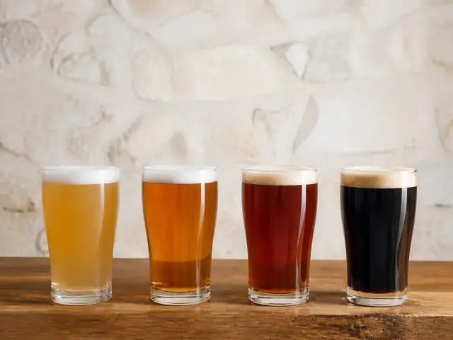 Quatre verres de bière alignés, de la plus pâle à la plus foncée, sur un comptoir en bois