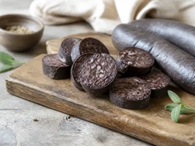 Tranches de boudin noir posées sur une planche en bois, la coupe sombre et granuleuse bien visible