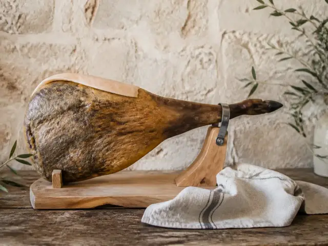 Jambon sec entier posé sur un support, la zone de coupe recouverte de sa couenne et de son gras