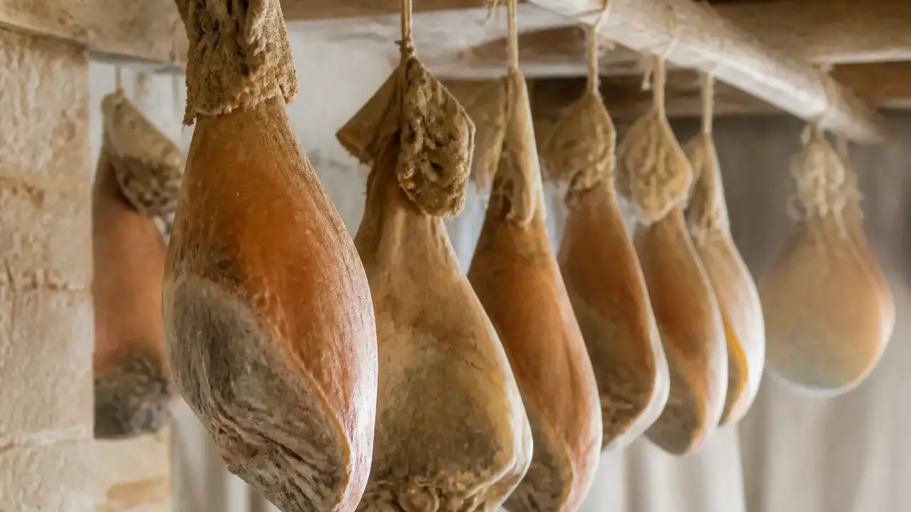 Jambon sec entier avec os, couenne dorée et pied, suspendu dans un séchoir