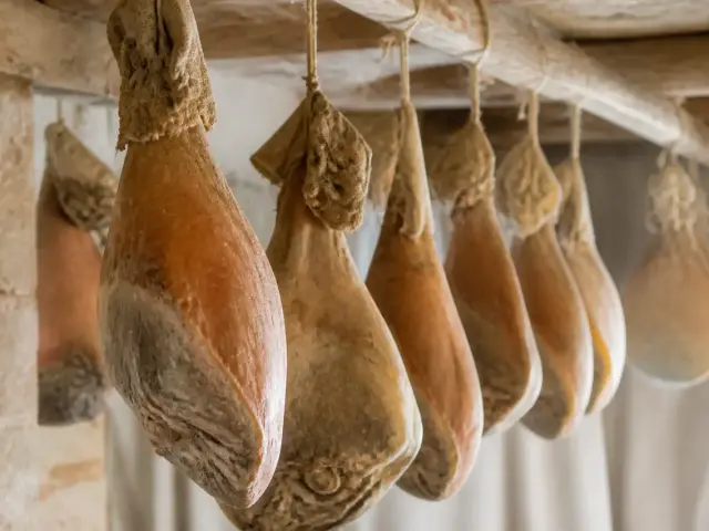 Jambon sec entier avec os, couenne dorée et pied, suspendu dans un séchoir