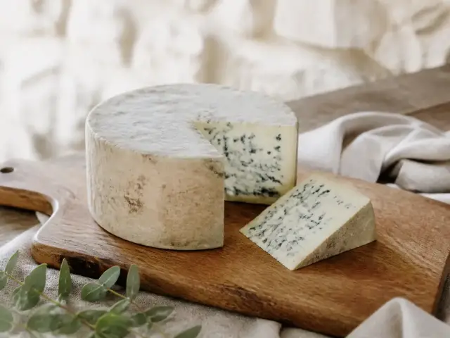 Fourme cylindrique à croûte grise entamée, tranche de pâte crème veinée de bleu